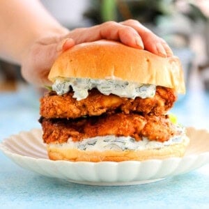 a hand pressing one tandoori chicken sandwich on a white plate.
