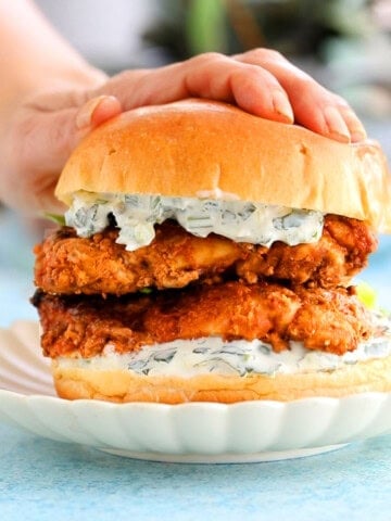 a hand pressing one tandoori chicken sandwich on a white plate.