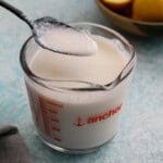 one black spoon full of white buttermilk above a glass measuring cup.