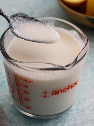 one black spoon full of white buttermilk above a glass measuring cup.