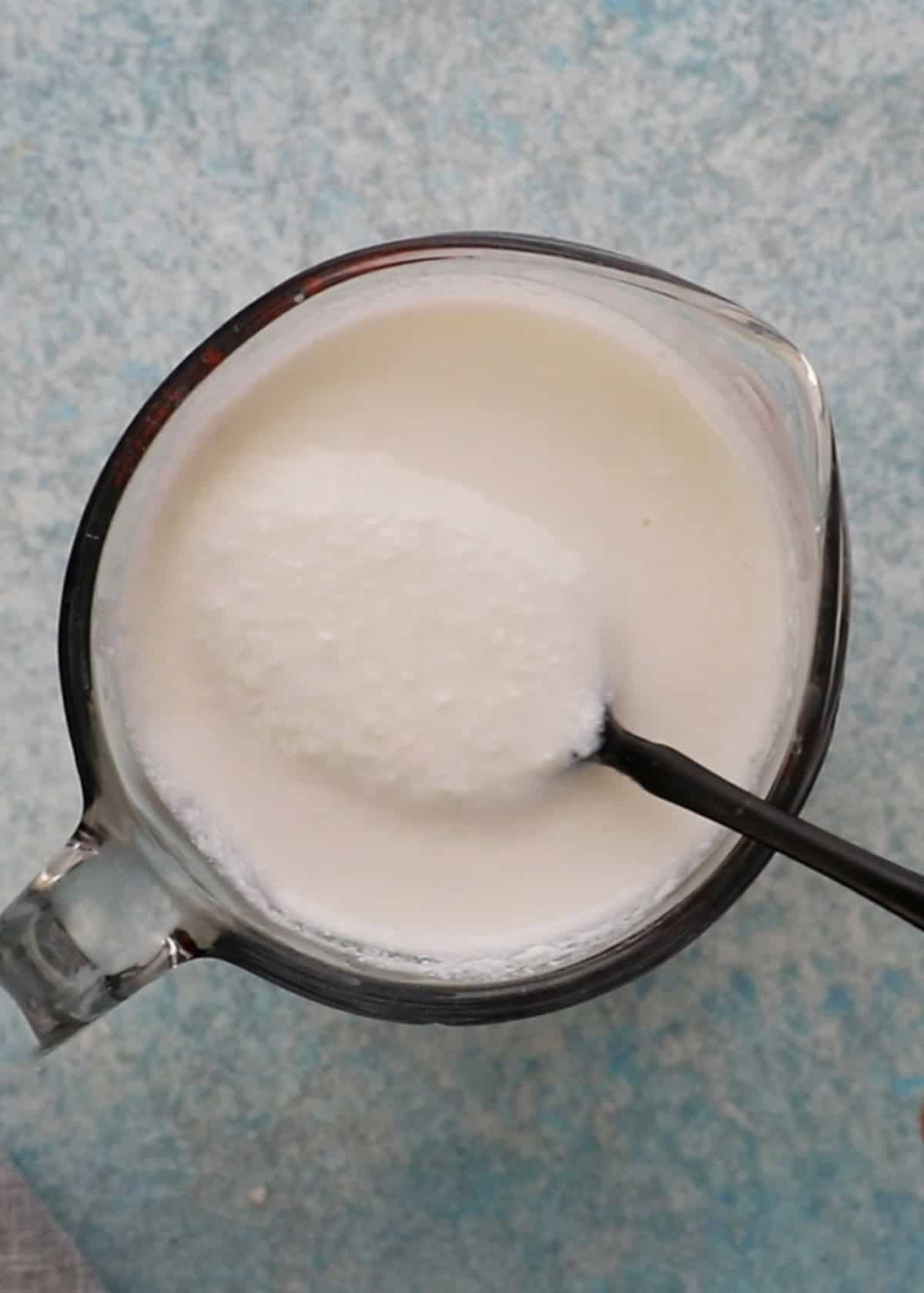 a hand holding a spoonful of white buttermilk in a glass measuring cup.