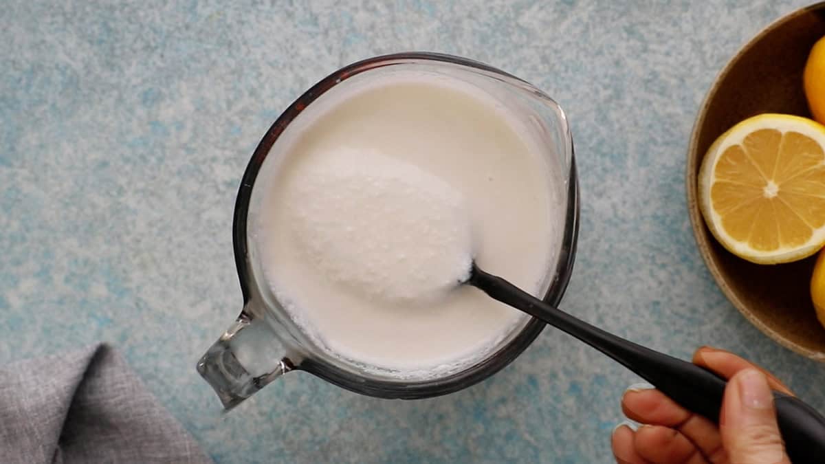 a hand holding a spoonful of white buttermilk in a glass measuring cup.