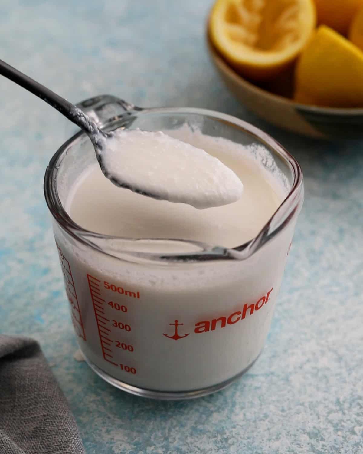 one black spoon full of white buttermilk above a glass measuring cup.
