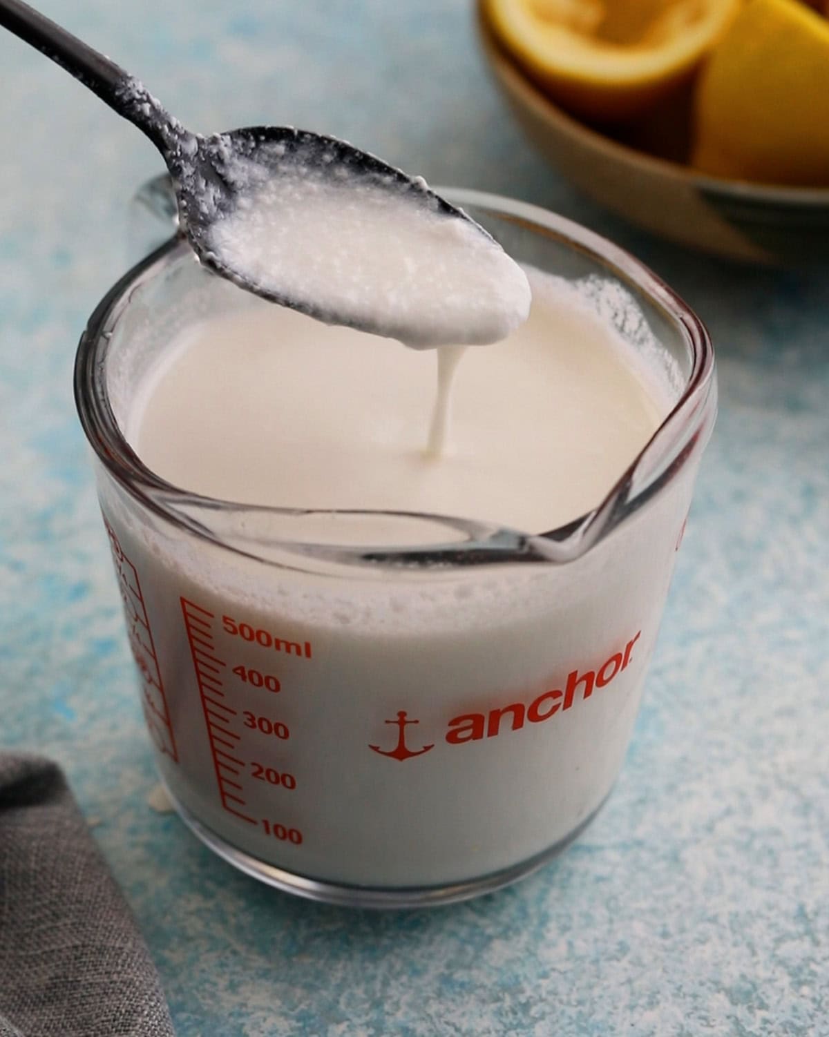 one black spoon full of white buttermilk above a glass measuring cup.