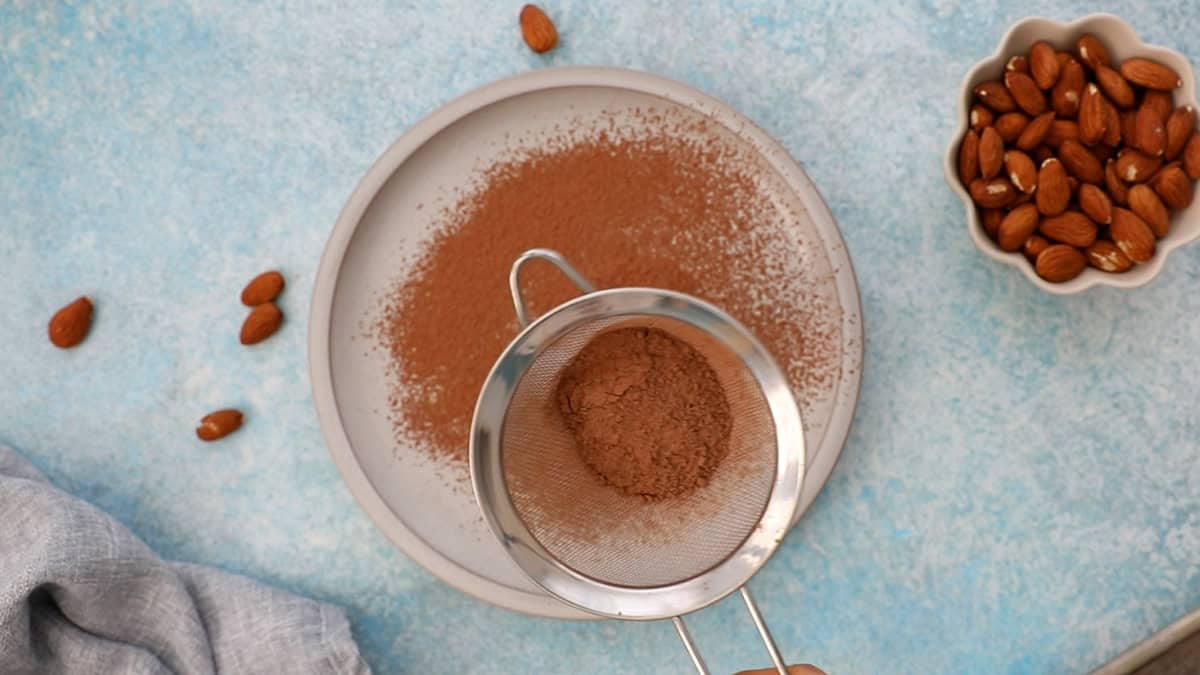 a metal strainer with brown cocoa powder in a white plate.
