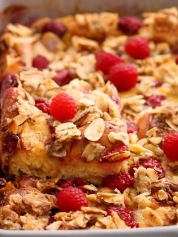 yellow french toast casserole topped with pink raspberries in a grey dish.