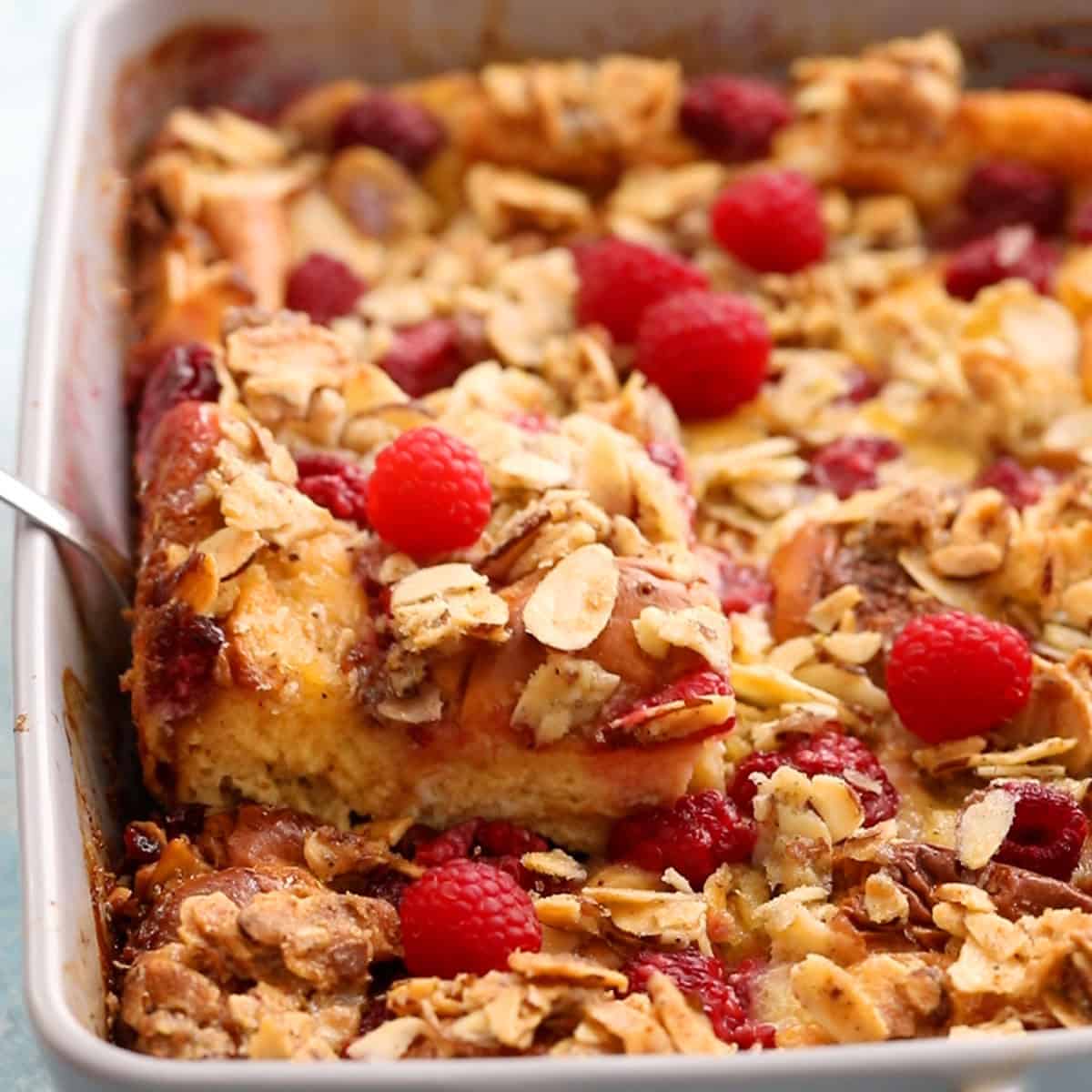 yellow french toast casserole topped with pink raspberries in a grey dish.