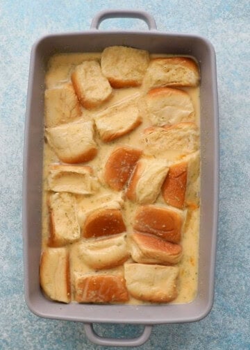 chopped bread soaking in yellow custard in a grey dish.