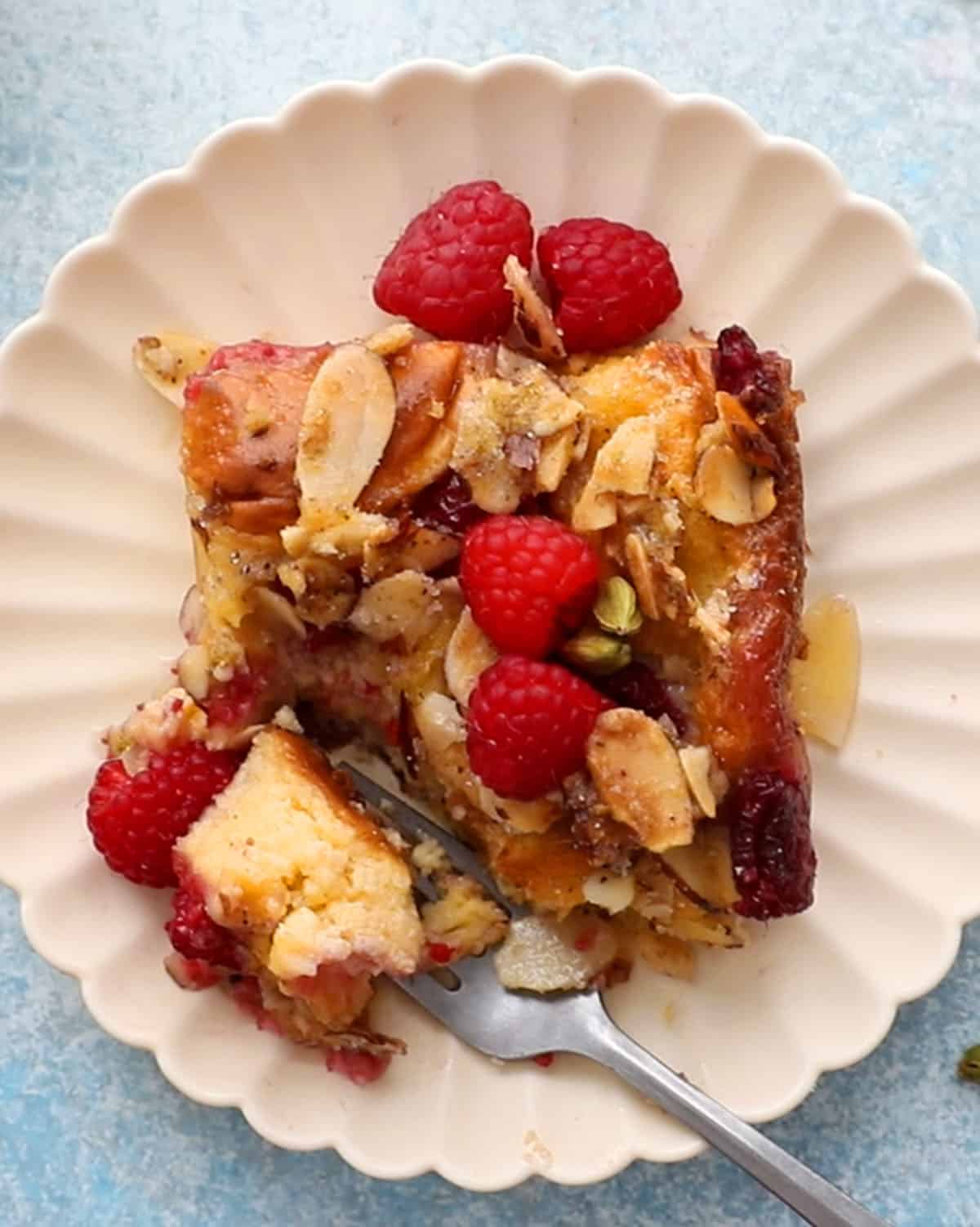 one slice of baking raspberry french toast casserole in a fluted white plate along with a fork.