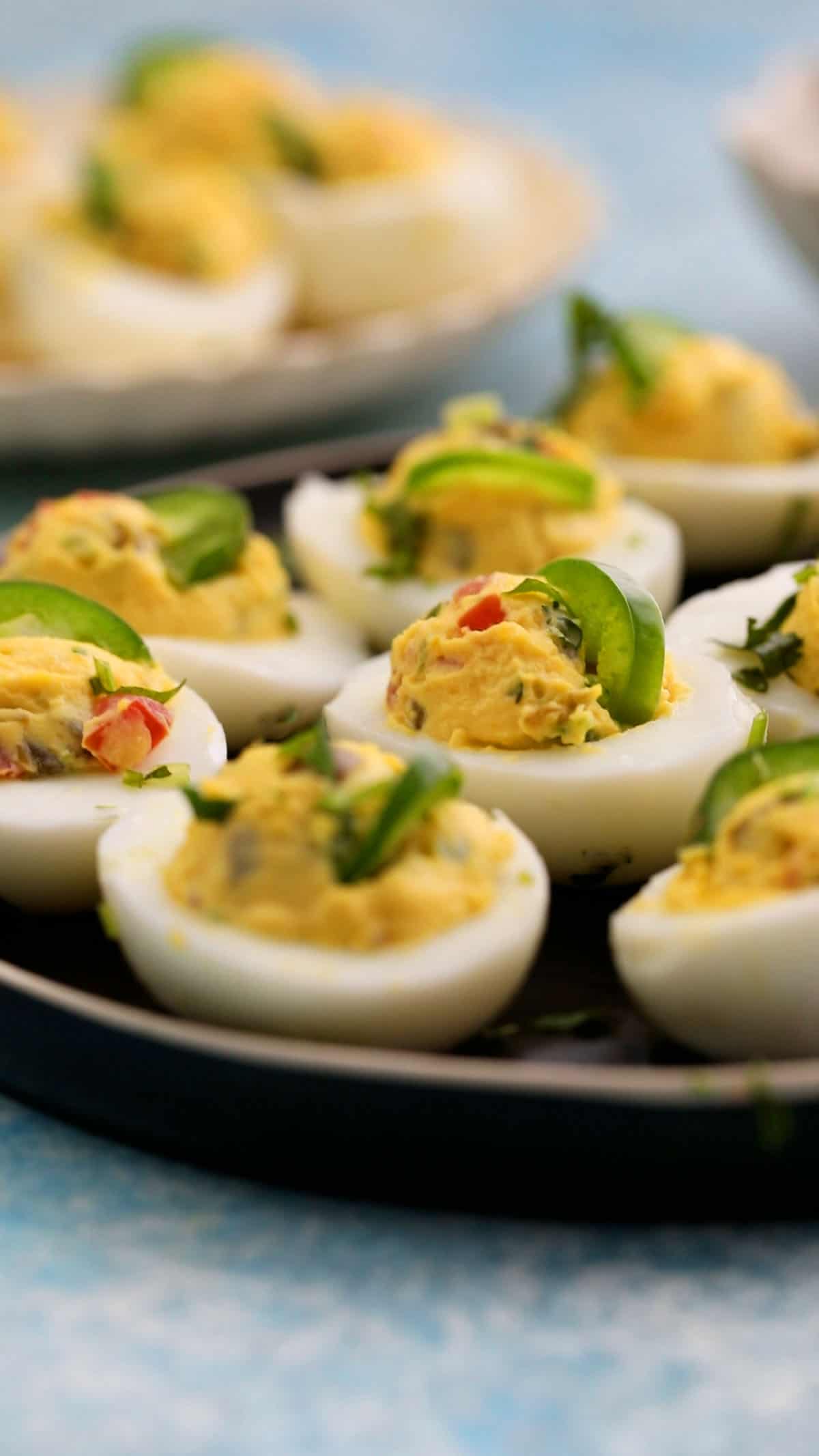 spicy deviled eggs garnished with green jalapenos in a black plate.