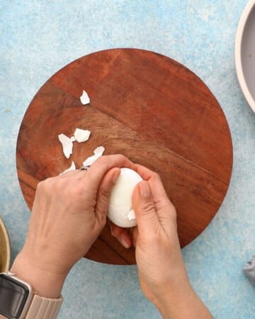two hands peeling one boiled egg.