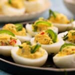 spicy deviled eggs garnished with green jalapenos in a black plate.