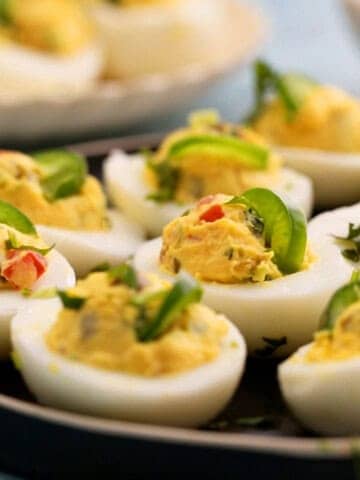 spicy deviled eggs garnished with green jalapenos in a black plate.