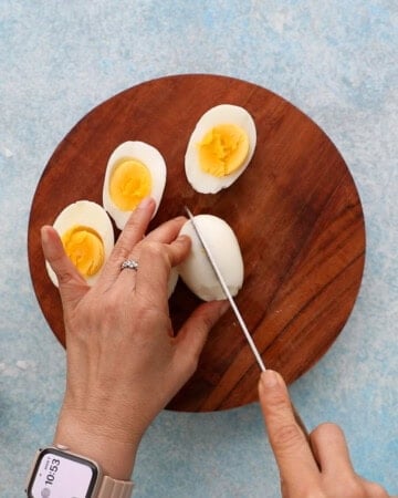 two hands cutting boiled eggs in half.