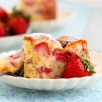 one slice of strawberry cake in a white fluted bowl along with one pink strawberry.