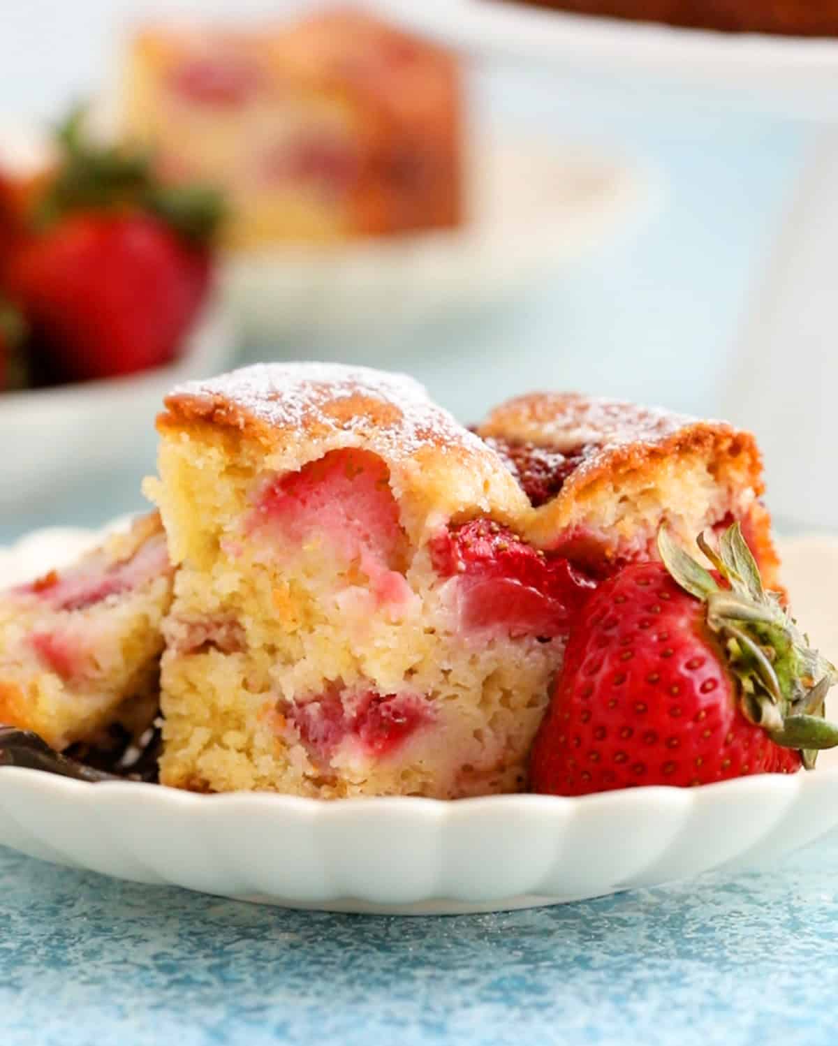 one slice of strawberry cake in a white fluted bowl along with one pink strawberry.