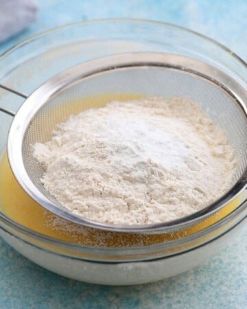 white flour in a metal sieve placed over a glass bowl.