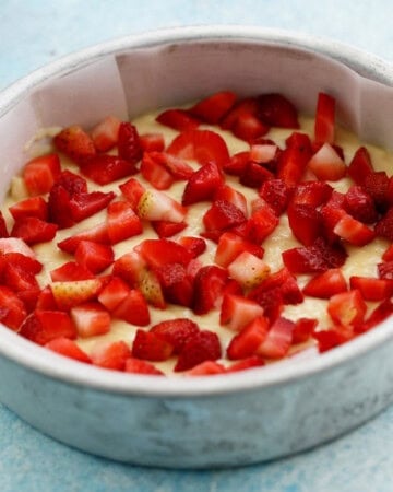 chopped pink strawberries topped over yellow cake batter in a round pan.