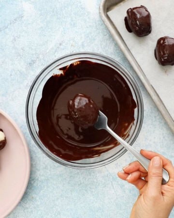 a hand dipping one almond joy date in a bowl or melted chocolate.