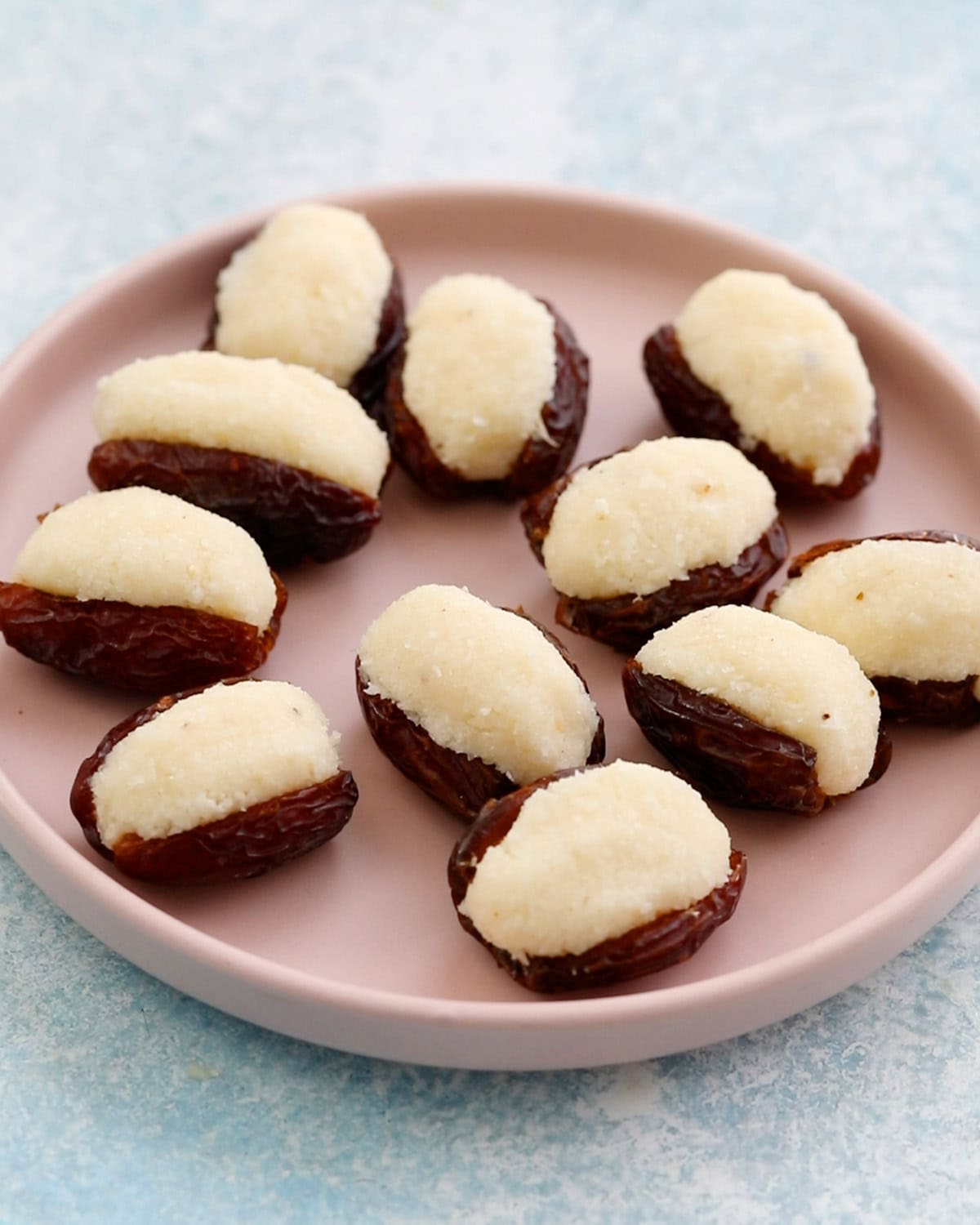 11 coconut stuffed dates placed in a pink plate.