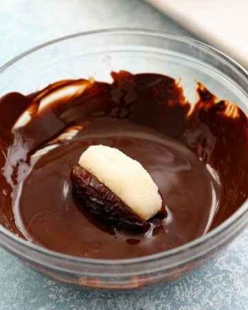 one coconut stuffed date in a bowl of melted chocolate.