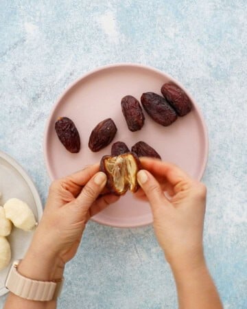 two hands removing the seed from a date.