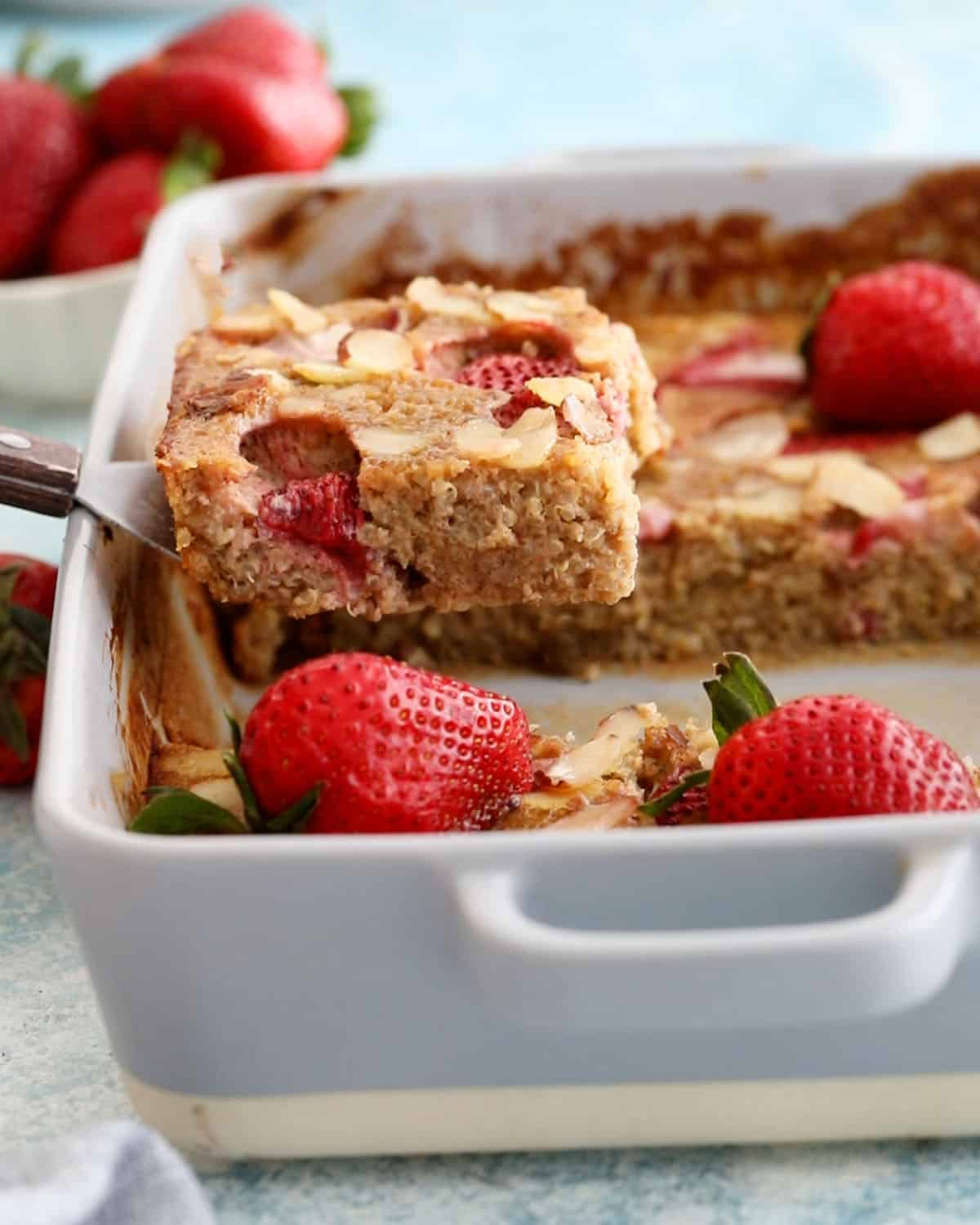 baked quinoa casserole in a grey baking dish topped with pink strawberries.