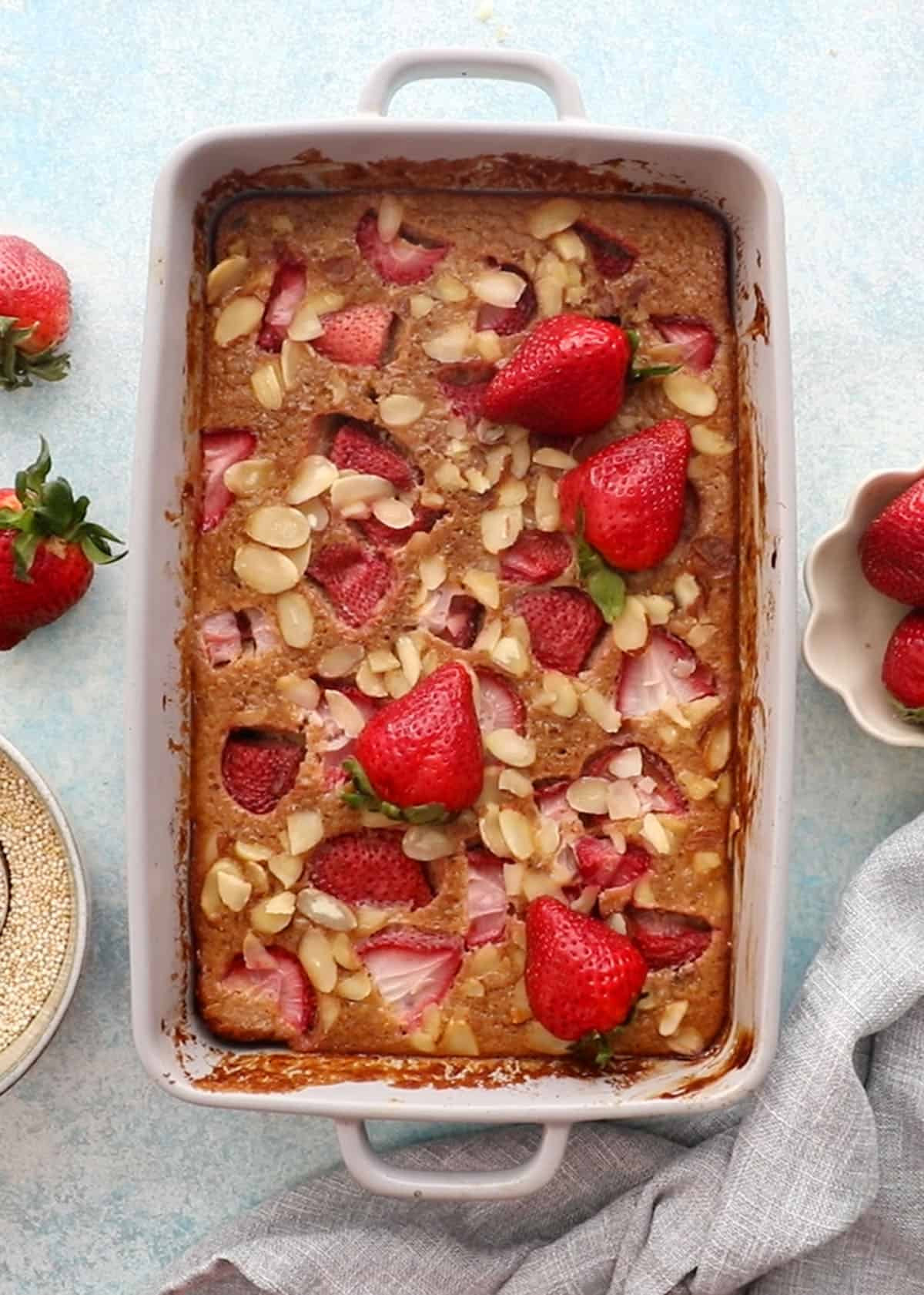 baked quinoa casserole in a grey baking dish topped with pink strawberries.