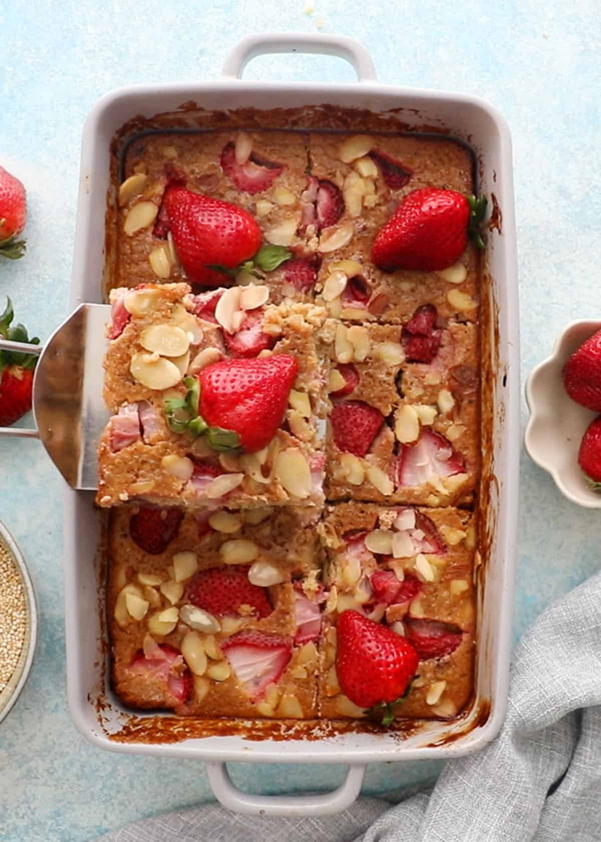 baked quinoa casserole in a grey baking dish topped with pink strawberries.