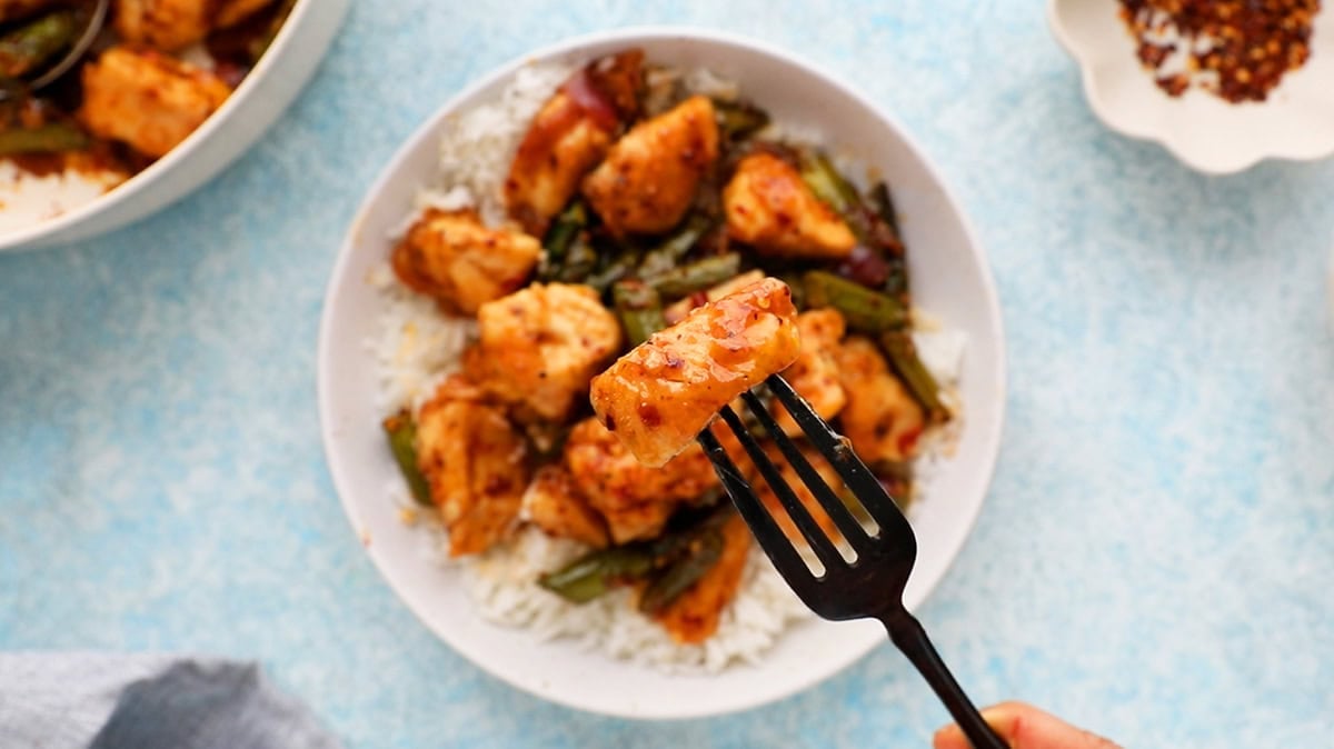 cooked chicken and green asparagus in a white bowl along with a black fork.