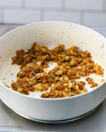 brown onion mixture cooking in a white skillet.