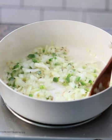 chopped onion and green chili cooking in a white skillet.