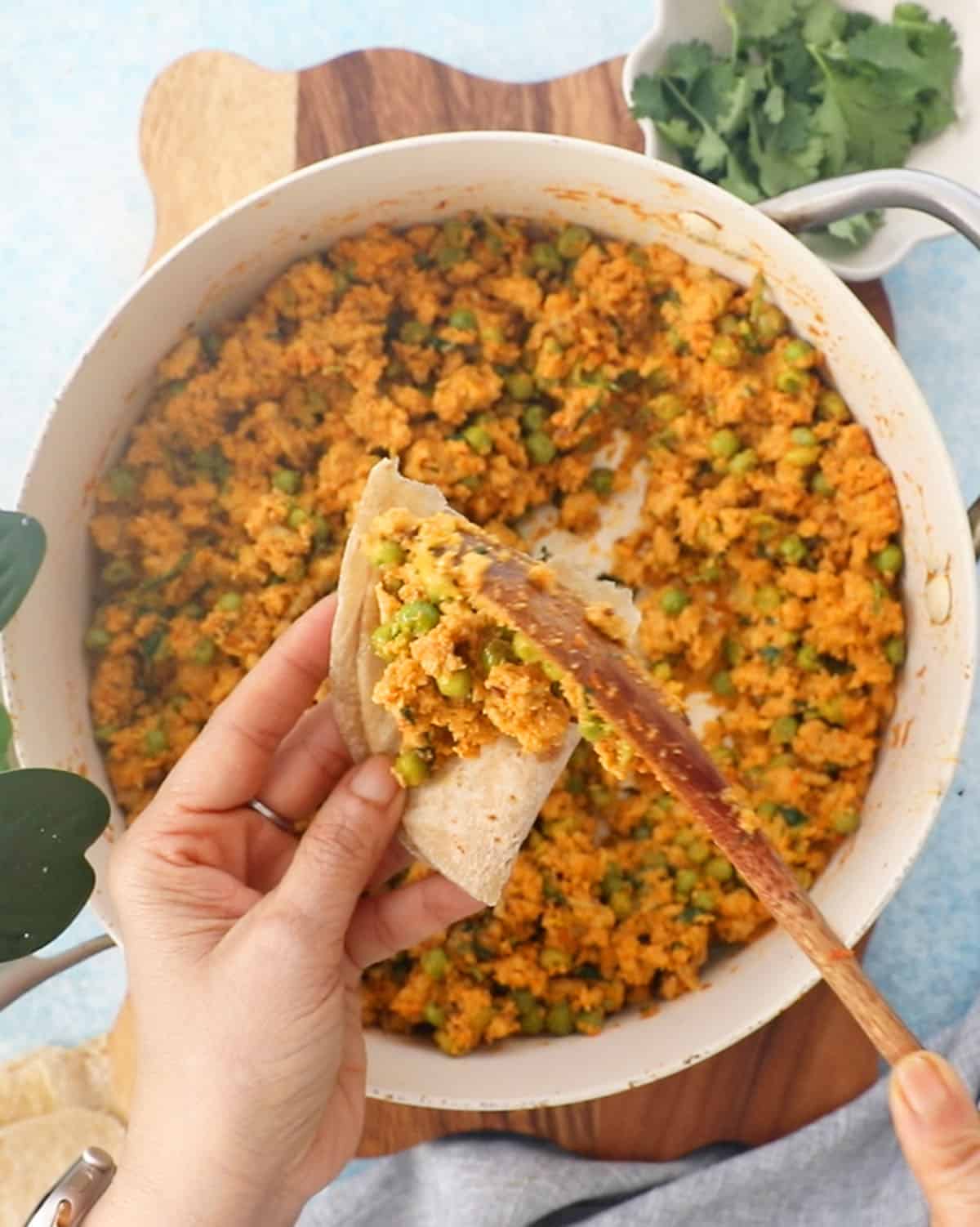 two hands scooping up soem chicken keema into a piece of brown flat bread.