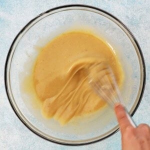 a hand whisking eggs in a glass bowl.