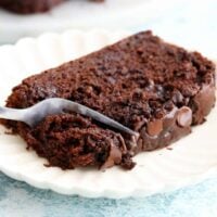 a fork cutting into a slice of brown chocolate zucchini bread in a white plate.