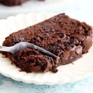 a fork cutting into a slice of brown chocolate zucchini bread in a white plate.