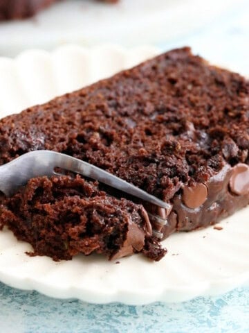 a fork cutting into a slice of brown chocolate zucchini bread in a white plate.