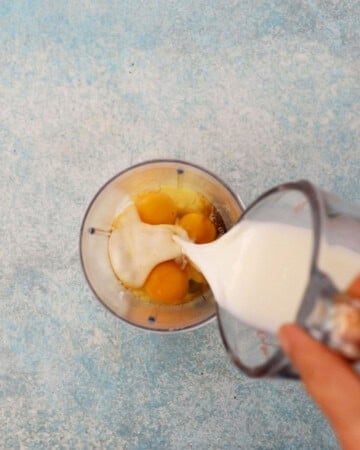 a hand pouring white milk into a blender jar.