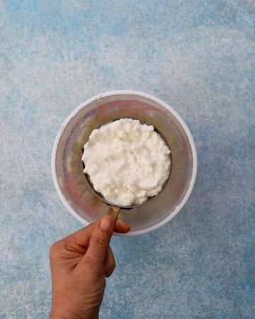 a hand holding one cup of cottage cheese.