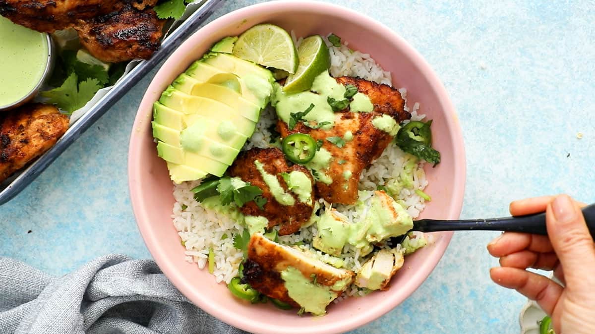 Peruvian chicken, avocado, rice and green sauce in a pink bowl.