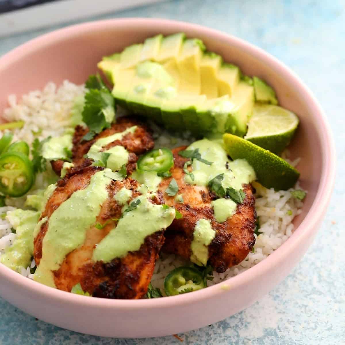 peruvian chicken thighs with white rice and green sauce in a pink bowl.