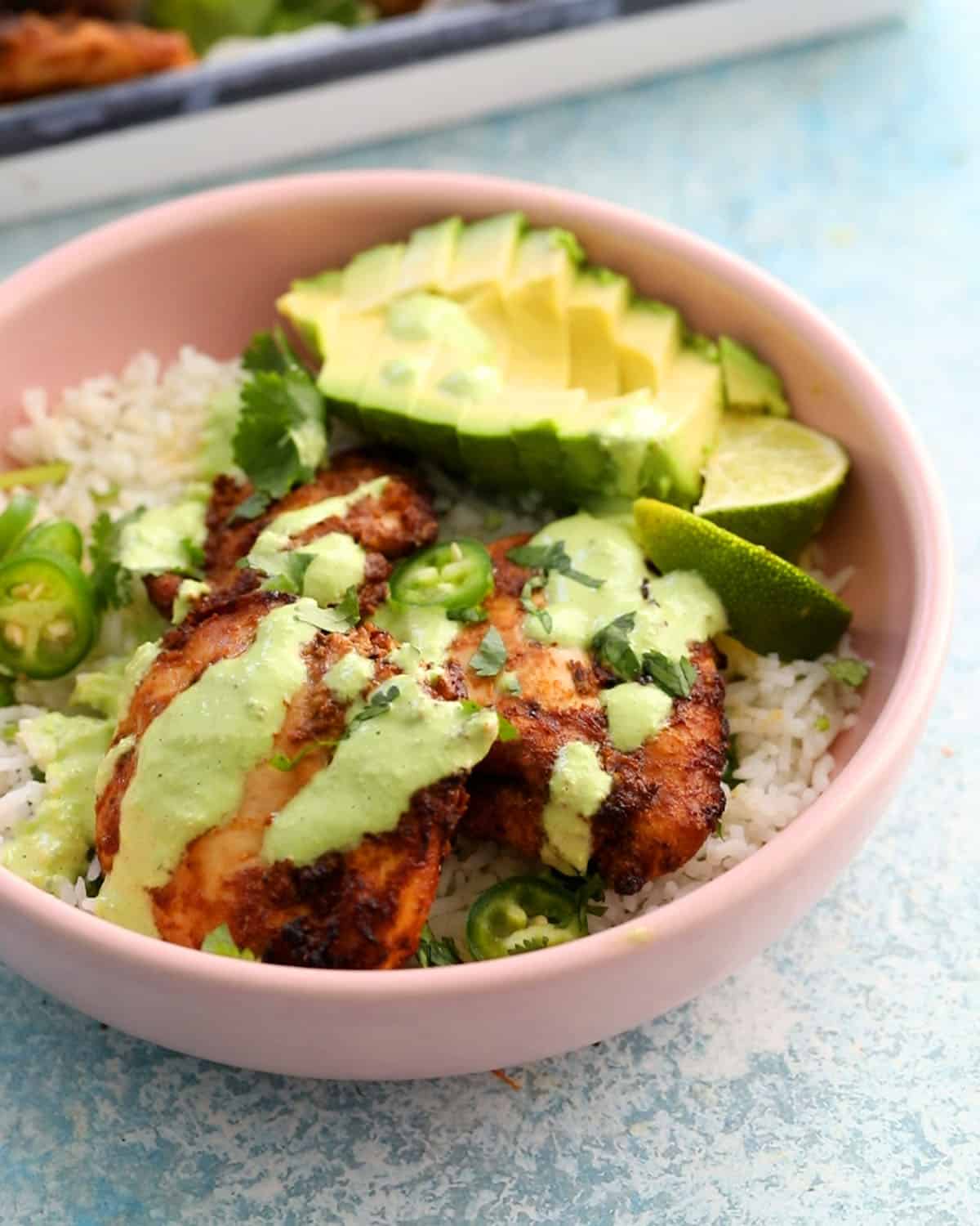 Peruvian chicken, avocado, rice and green sauce in a pink bowl.