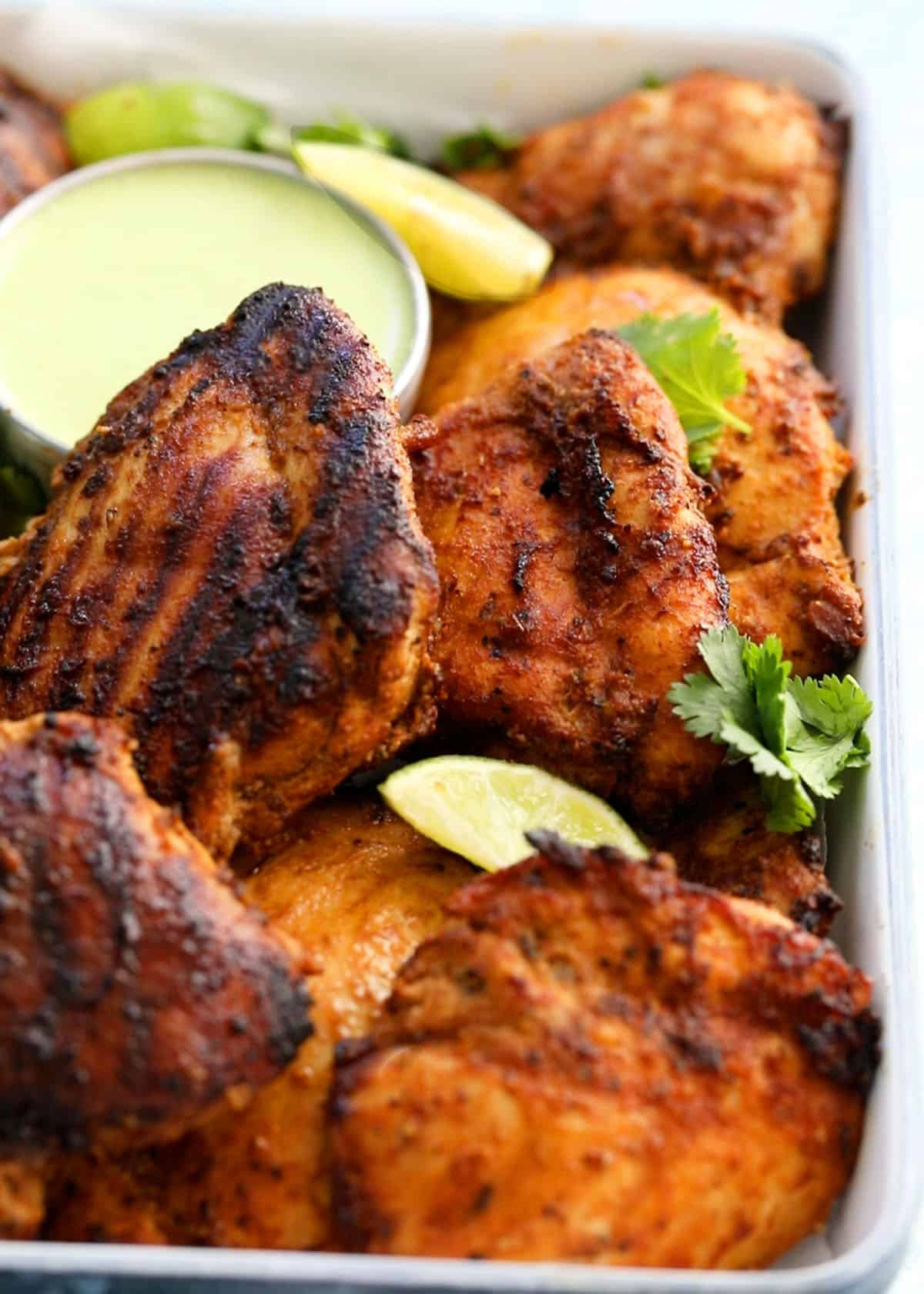 cooked Peruvian chicken thighs in a white tray along with green sauce.