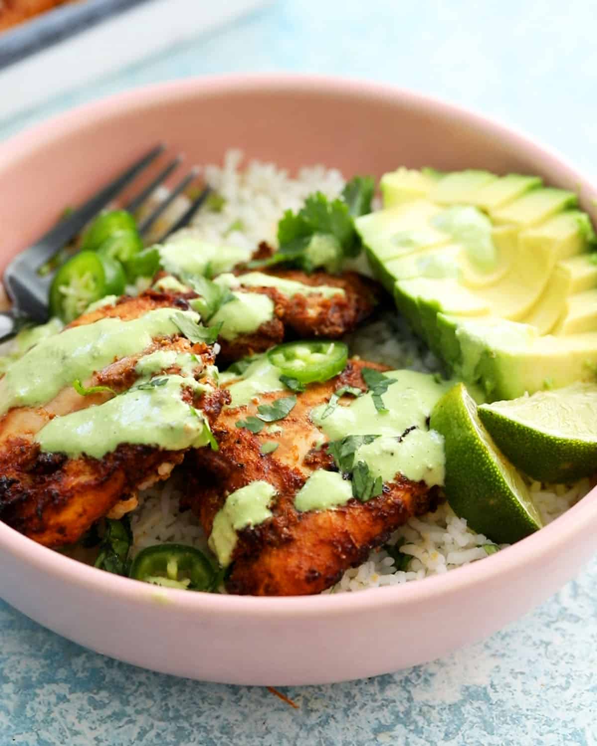 Peruvian chicken, avocado, rice and green sauce in a pink bowl.