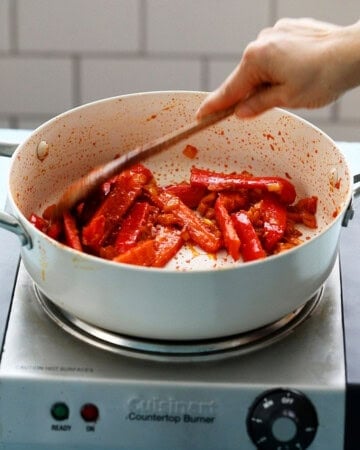 a hand cooking red pepper in a white pan.