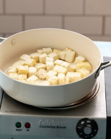 white tofu cubes cooking in a white pan.