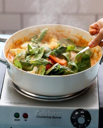 a hand cooking green spinach in tofu curry in a white pan.