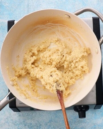 badam burfi cooking in a white pan.