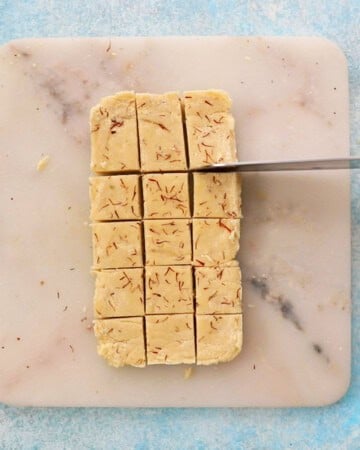 a hand cutting badam burfi in a white marble.