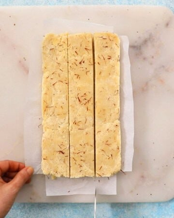 a hand cutting badam burfi in a white marble.